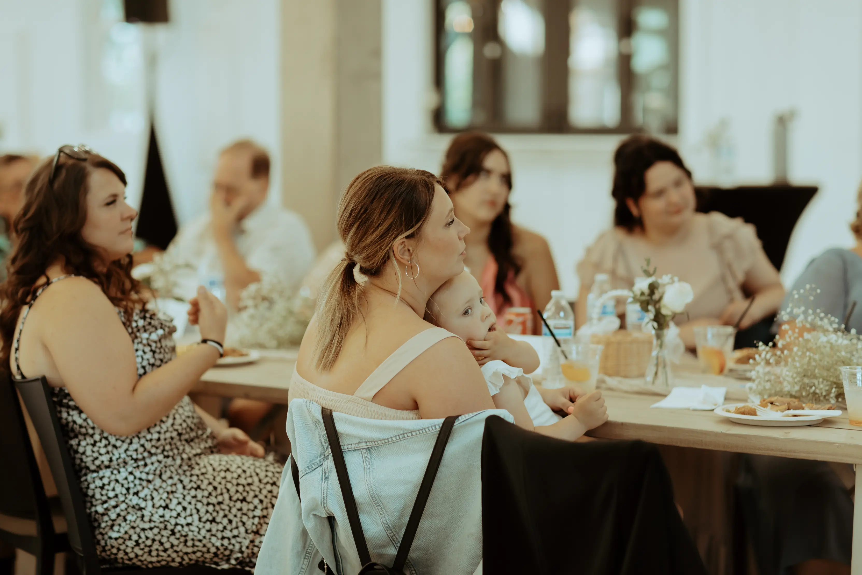Wedding guests and a mother holding her child during the reception at Sage and Social wedding venue, enjoying heartfelt moments around a beautifully decorated table.