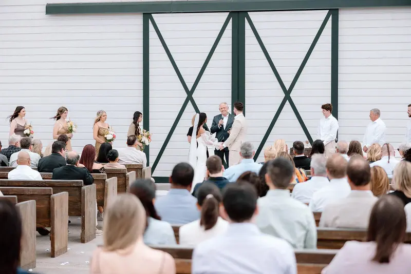 Savanna and Angler exchanging vows during their wedding ceremony at Butler Barn, with guests seated in front of the venue's iconic white barn doors.