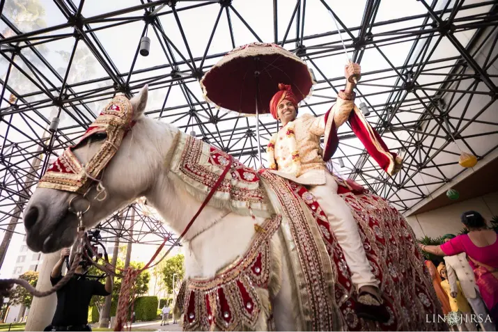 Indian groom riding a beautifully decorated white horse during the baraat procession, featured in the Indian Wedding Guide on Indian wedding traditions.