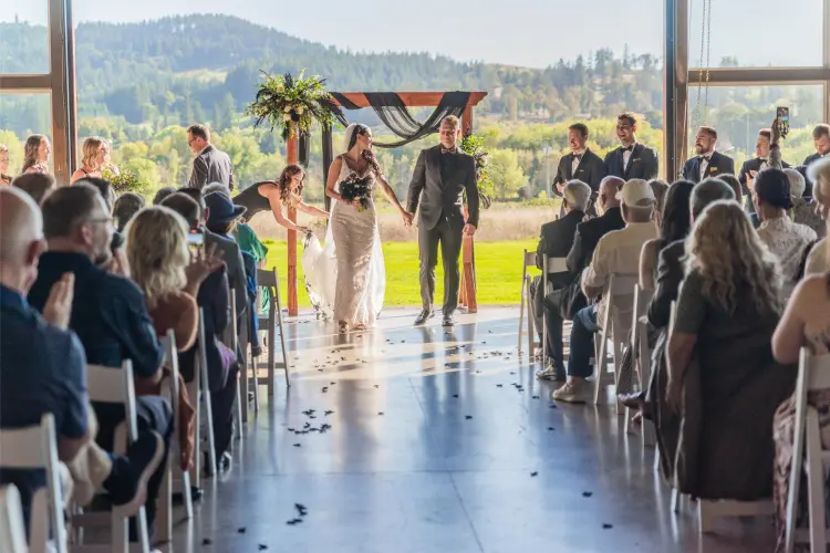 Bride and groom walking down the aisle after their ceremony at Water Oasis in Newberg, Oregon, surrounded by guests and panoramic countryside views.
