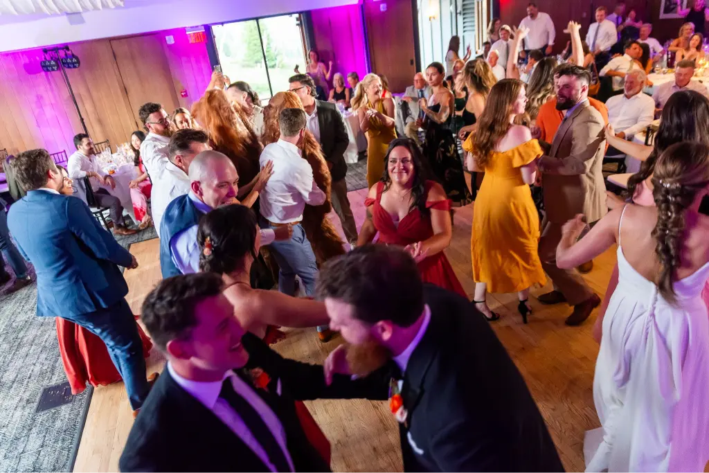 Wedding guests celebrating and dancing during a lively reception at Timberline Lodge with colorful DJ lighting and a packed dance floor.