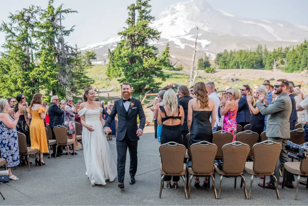Newly married couple walking down the aisle after their outdoor Timberline Lodge wedding ceremony with Mount Hood in the background.