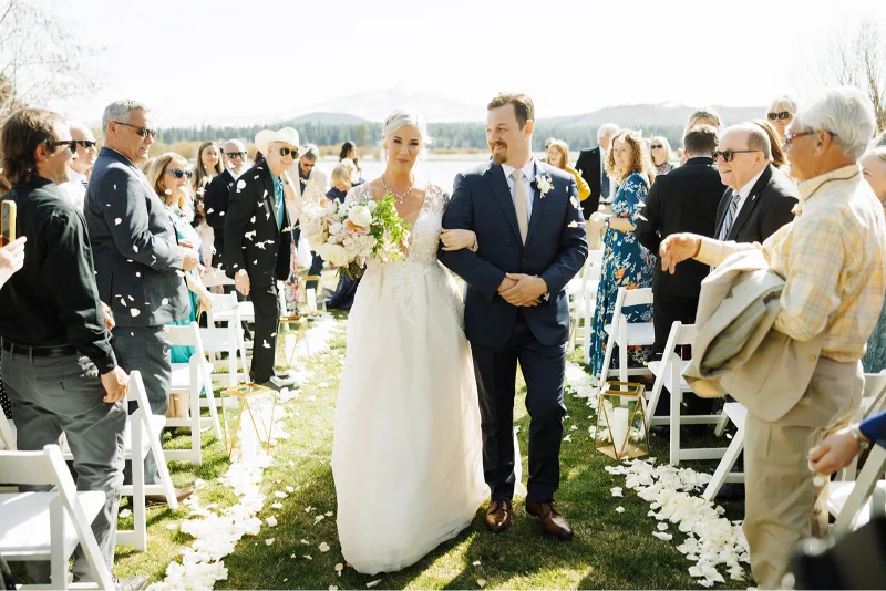 Newly married couple walking down the aisle after their Black Butte Ranch wedding ceremony as guests celebrate in Central Oregon.