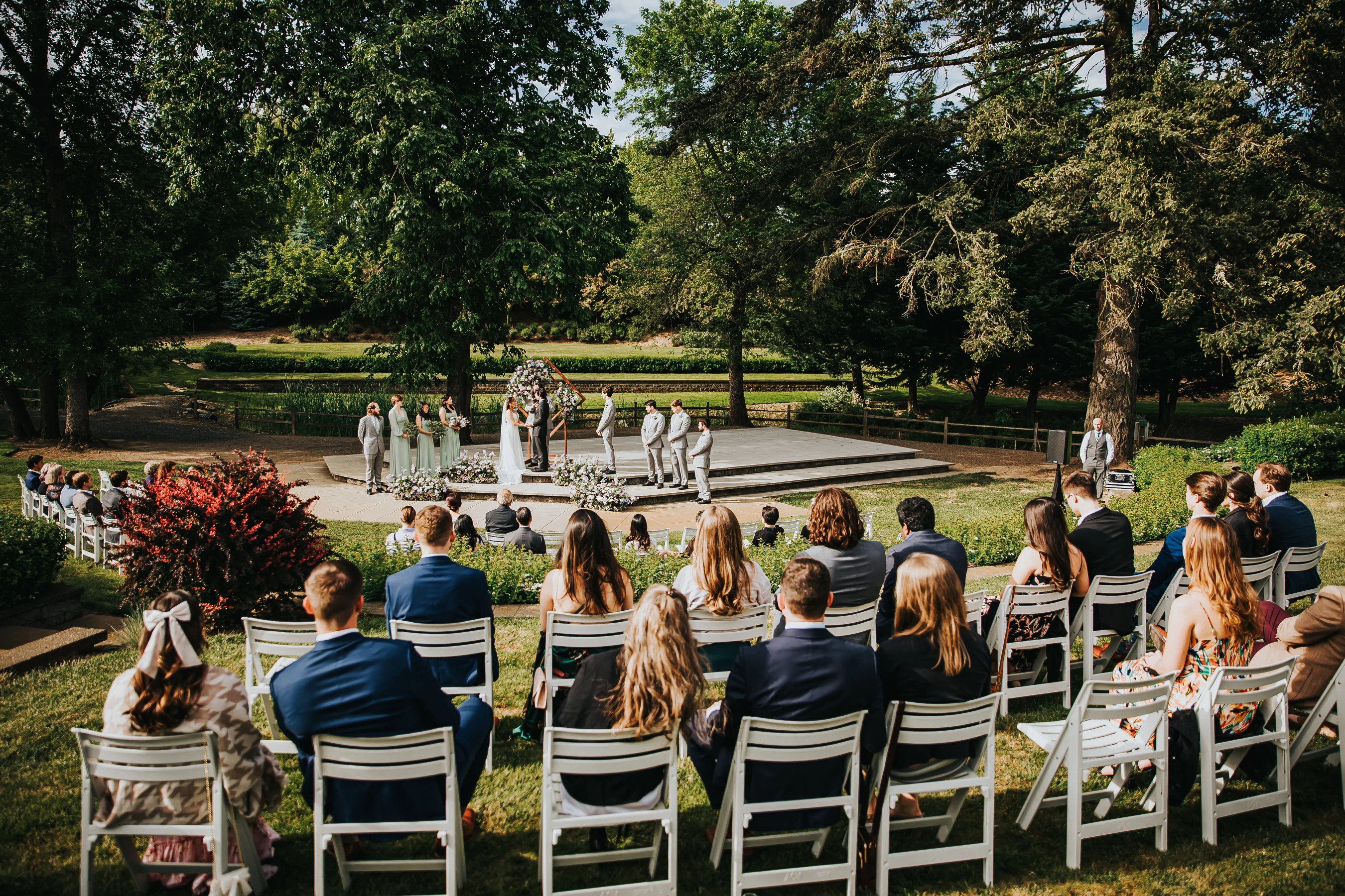 Guests watching an outdoor Aurora Vineyards wedding ceremony surrounded by gardens and towering trees in Oregon.