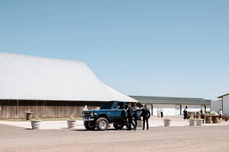 Vintage blue Ford Bronco arriving at Butler Barn wedding venue in Oregon before the outdoor wedding ceremony.