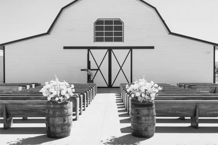 Outdoor wedding ceremony setup at Butler Barn with rustic wooden benches, white floral arrangements, and the iconic white barn in Oregon.