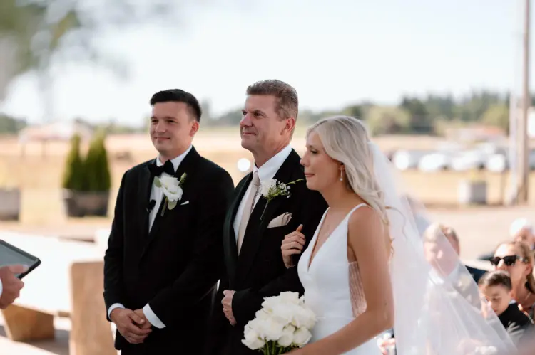 Bride walking down the aisle with her father during an outdoor Butler Barn wedding ceremony in Oregon.