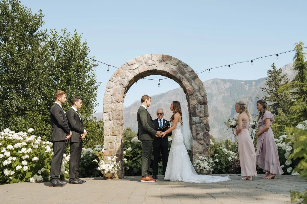 Bride and groom exchanging wedding vows beneath the iconic stone arch at Cape Horn Estate with Columbia River Gorge mountain views.