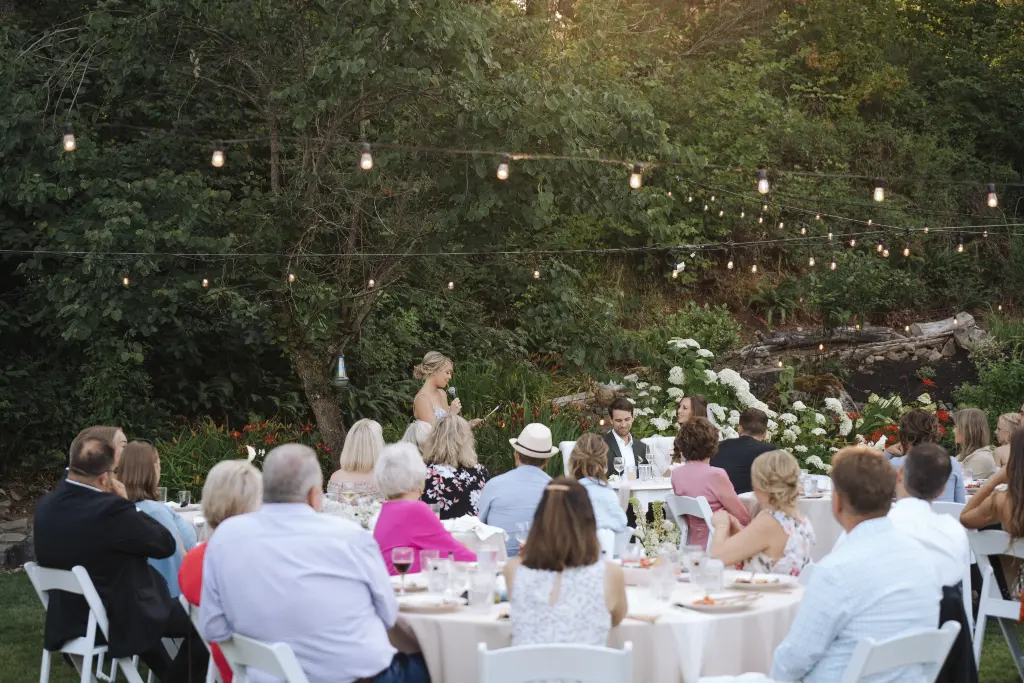 Outdoor wedding reception toast at Cape Horn Estate beneath café string lights surrounded by lush gardens in Washington.