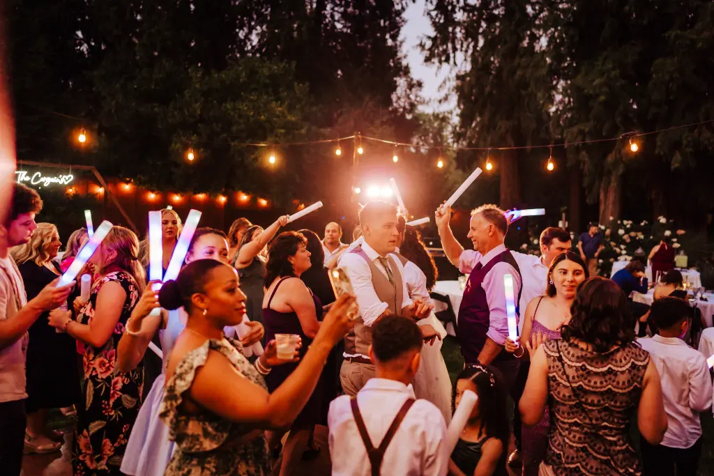 Wedding guests celebrating with colorful glow sticks on the dance floor during a fun outdoor evening reception at CedarVale Events.