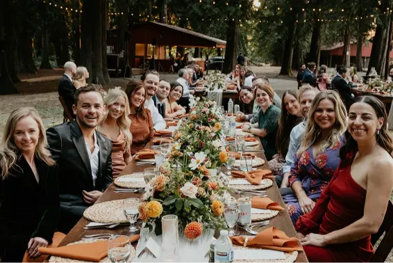 Guests gathered around a beautifully decorated reception table during a Wedding at Cedarville Lodge, surrounded by towering trees and elegant outdoor décor.