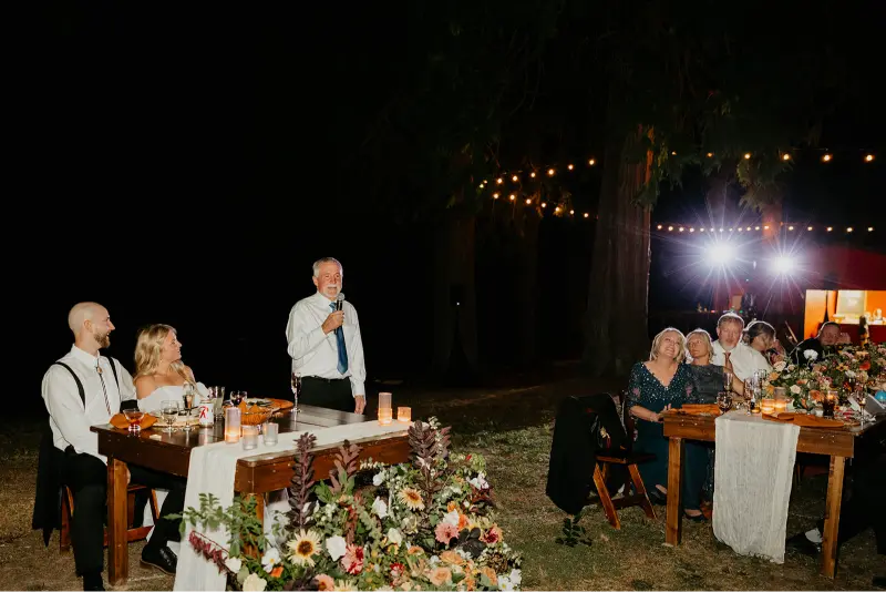 A family member giving a heartfelt wedding toast during an evening reception at a Wedding at Cedarville Lodge as the bride and groom listen with smiles.