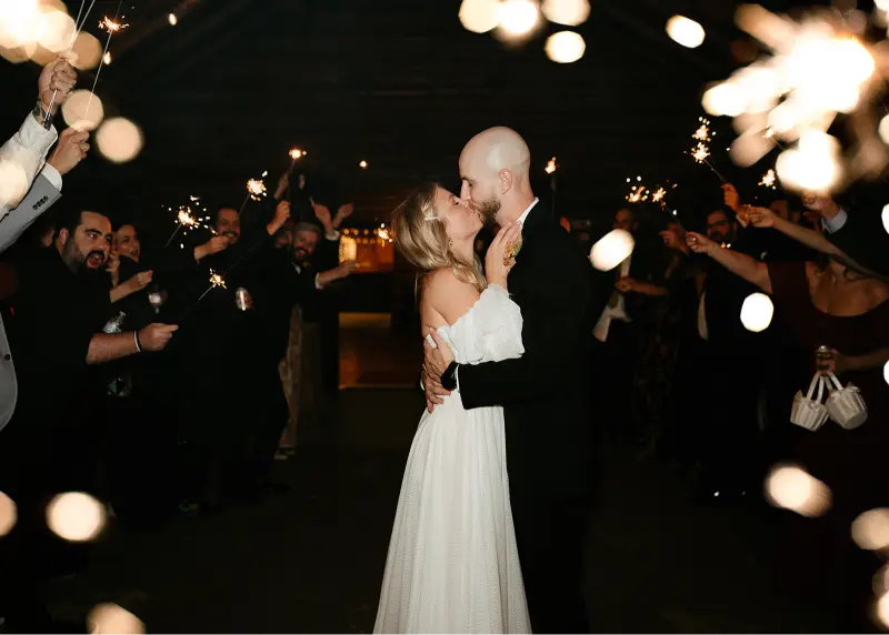 Bride and groom sharing a kiss during a sparkler exit at a Wedding at Cedarville Lodge, surrounded by cheering guests holding sparklers.