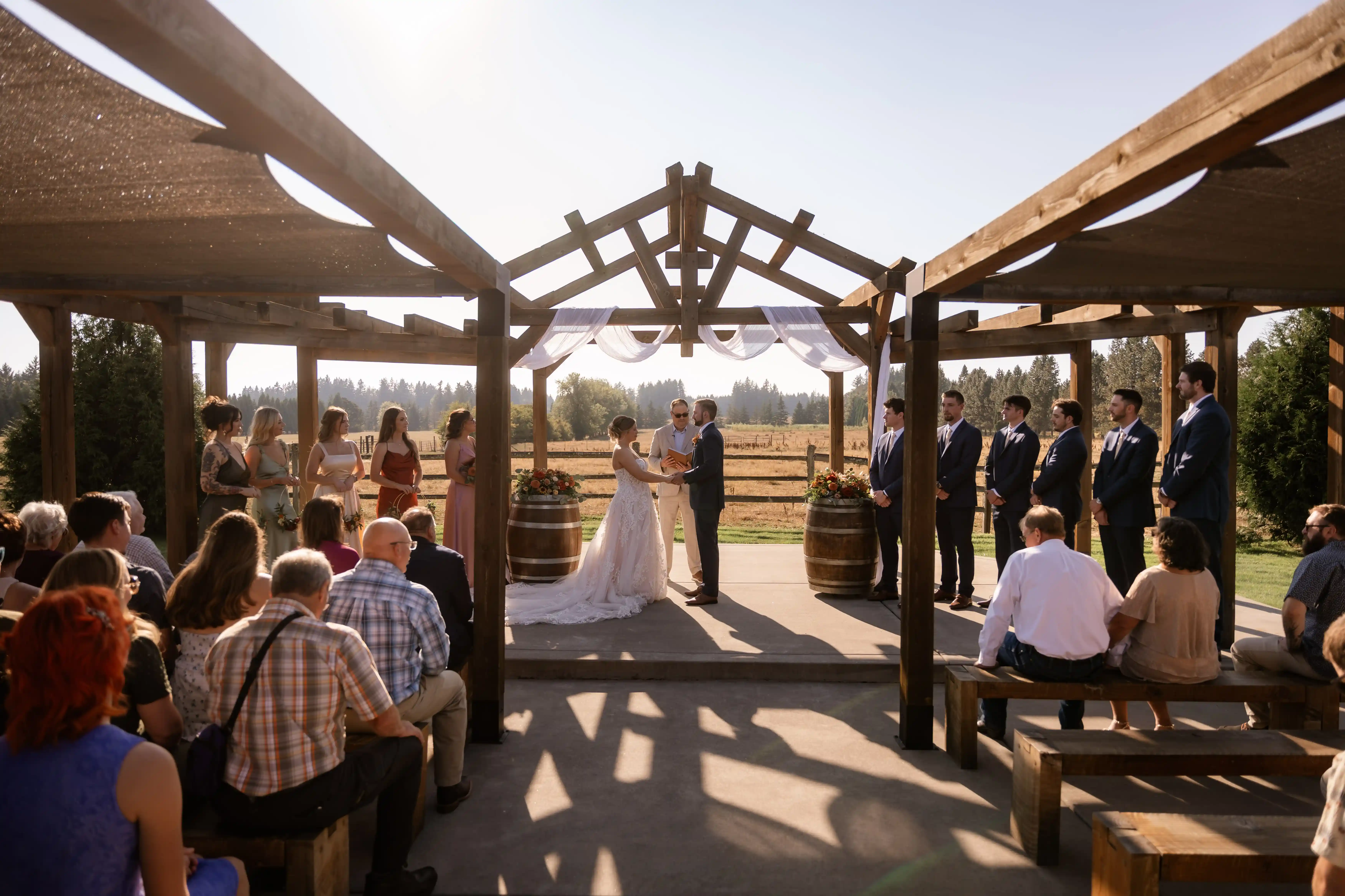 Outdoor-Jacquot-Vineyard-wedding-ceremony-with-the-bride-and-groom-exchanging-vows-beneath-a-rustic-wooden-pavilion-in-Oregon.