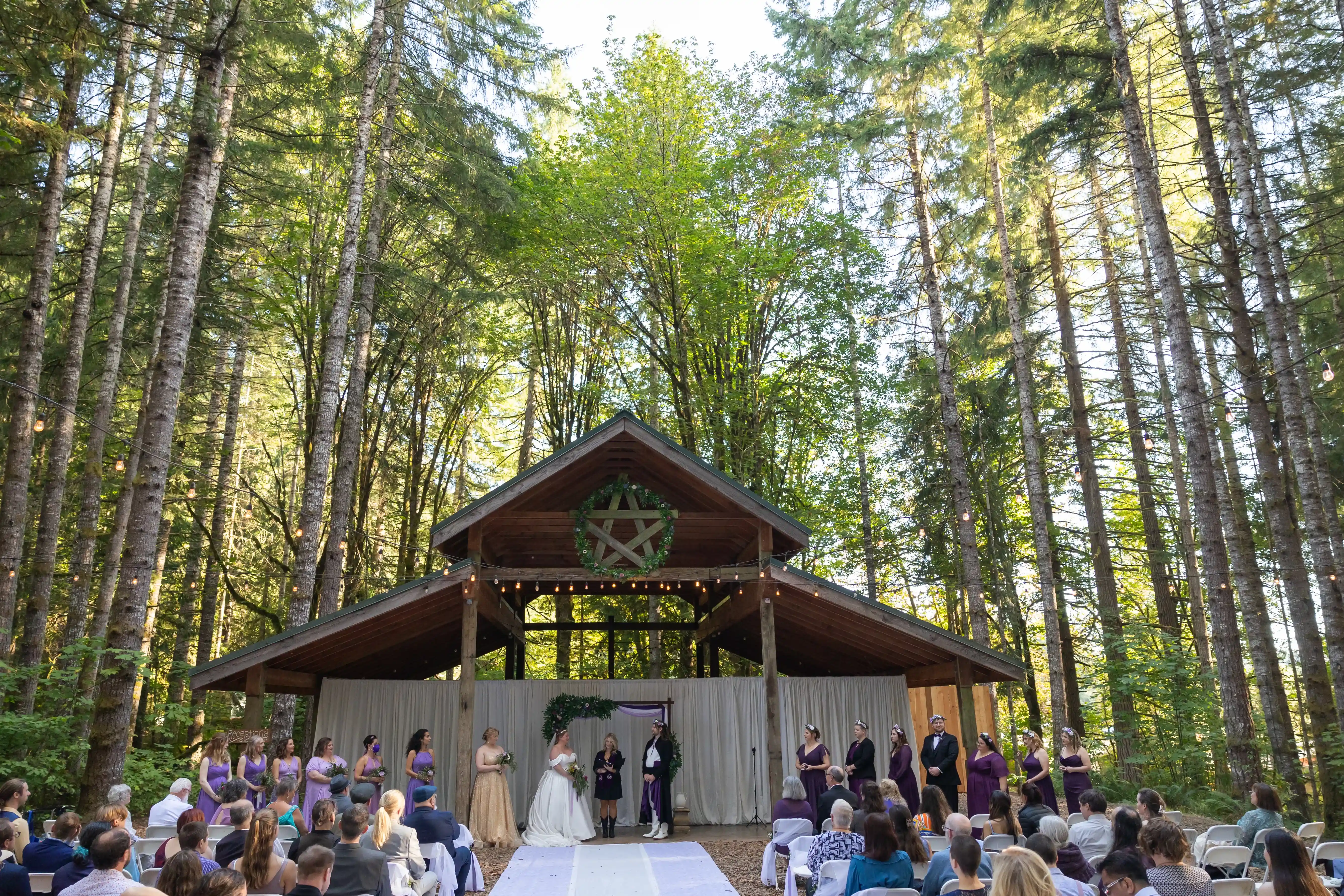 Outdoor-Hoyt-Arboretum-wedding-ceremony-in-Portland-with-the-bridal-party-standing-beneath-a-rustic-pavilion-in-a-forest-setting