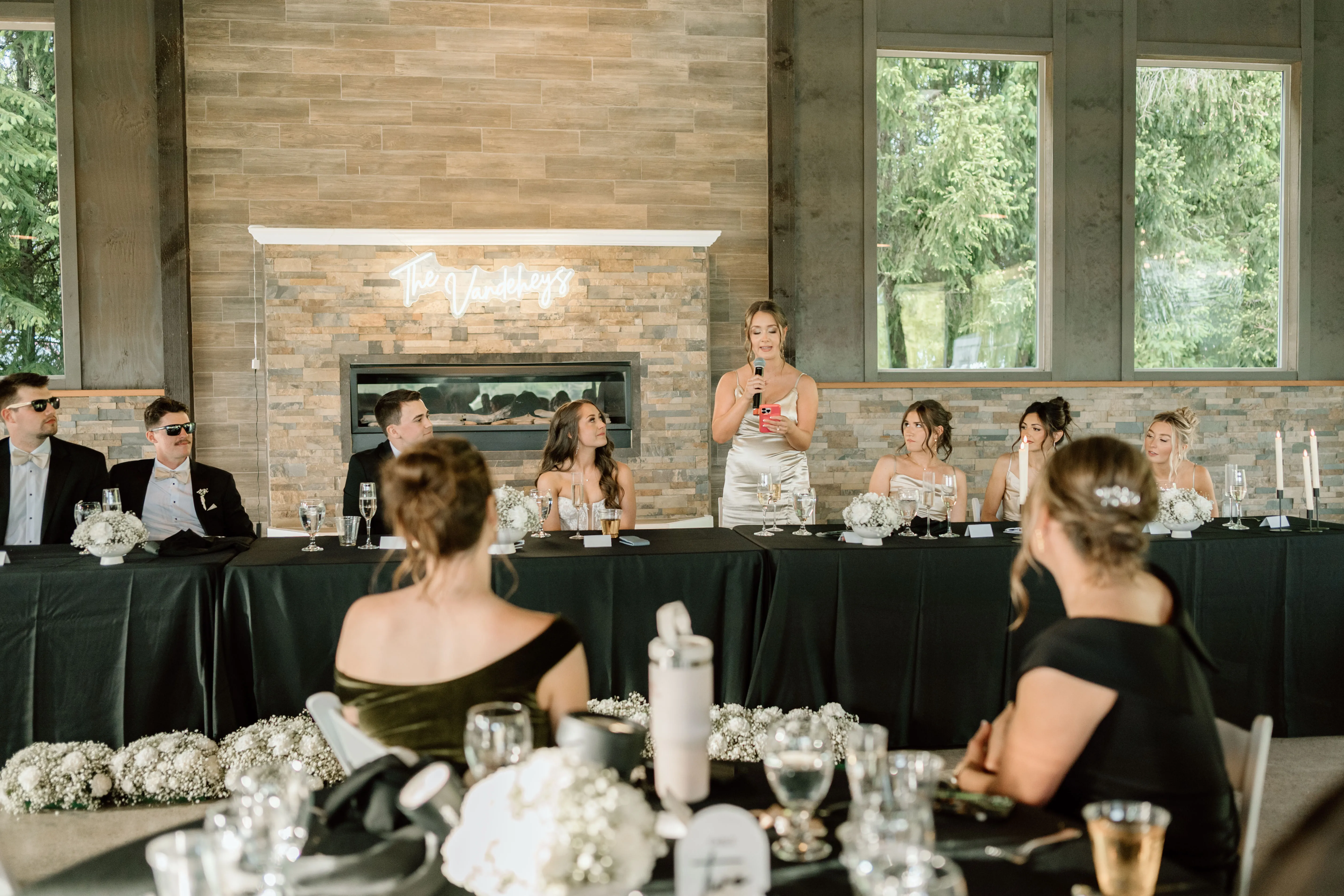 Bridesmaid delivering a heartfelt wedding toast at the head table during an elegant indoor wedding reception in Newberg, Oregon, as the bride, groom, and wedding party listen attentively.