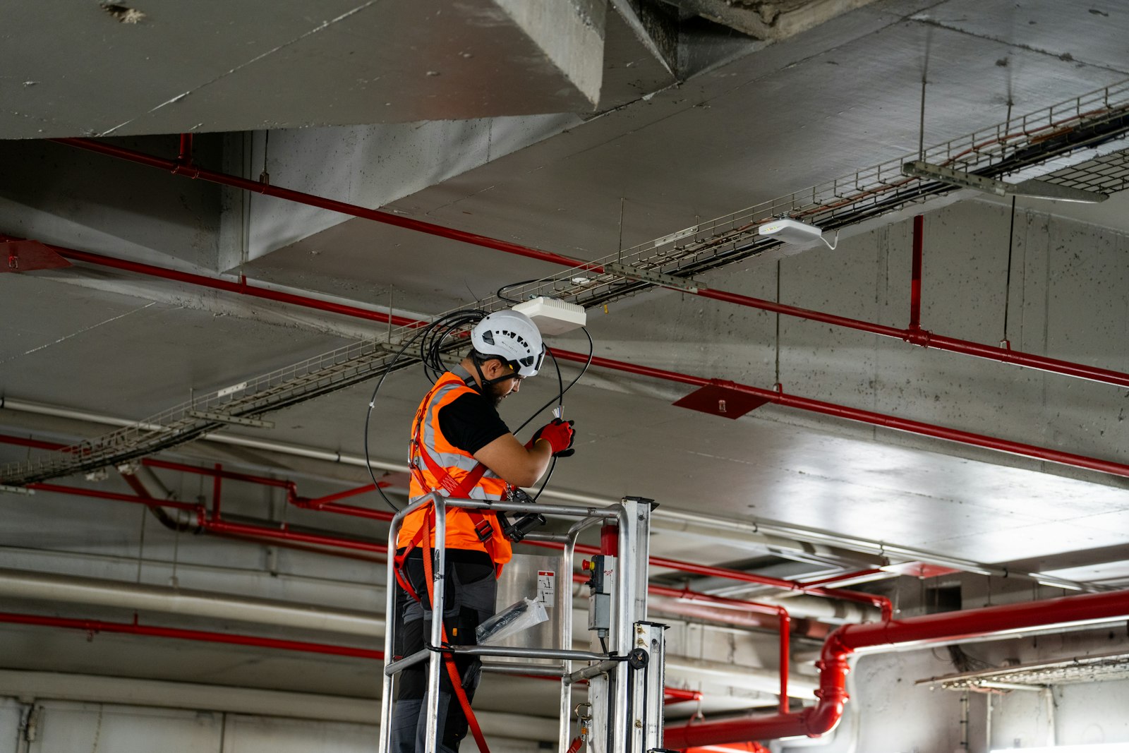 Tradesperson in a hard hat and hi-vis vest working from a lift inside a commercial building
