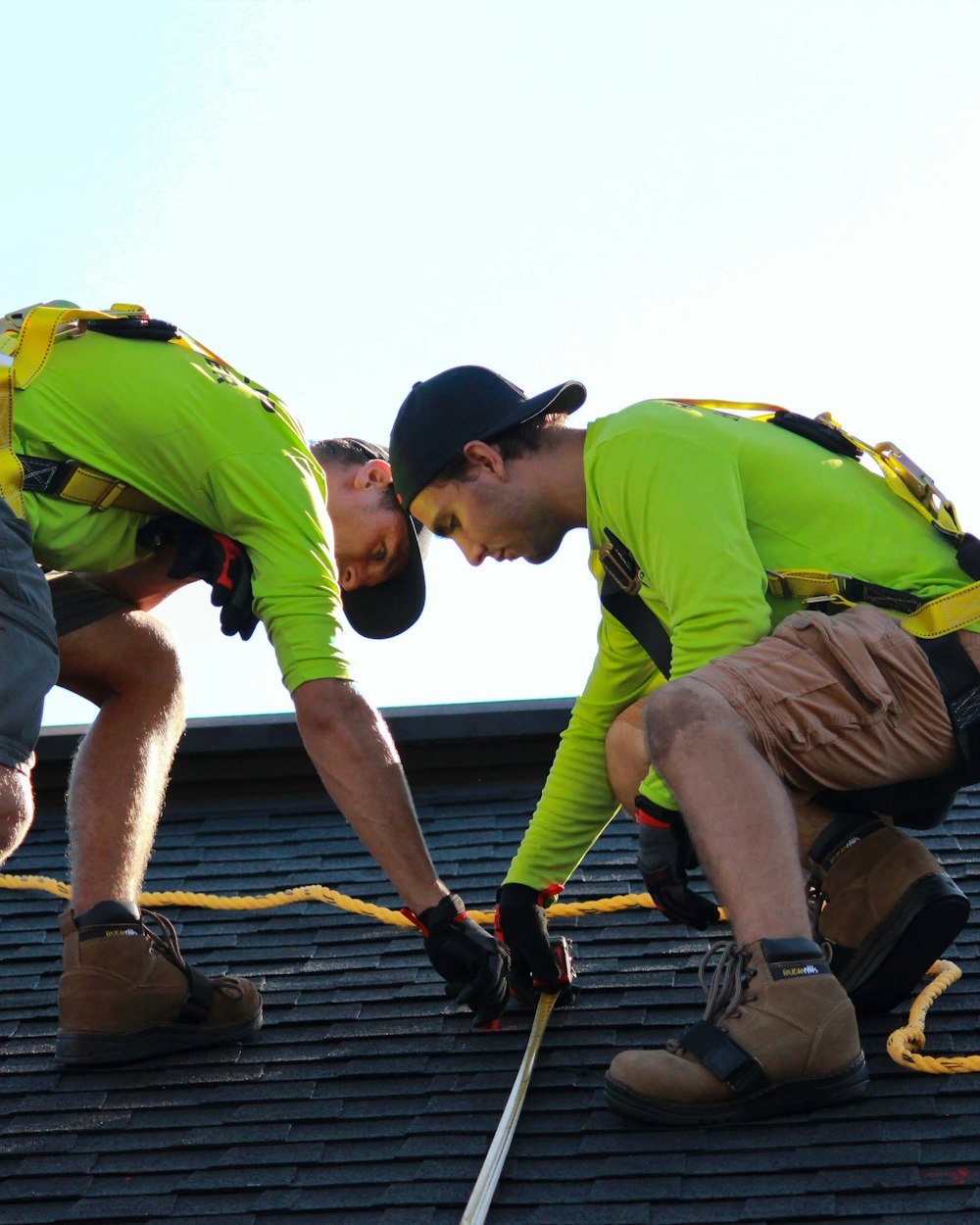 Two roofers in harnesses and hi-vis shirts measuring a shingle roof