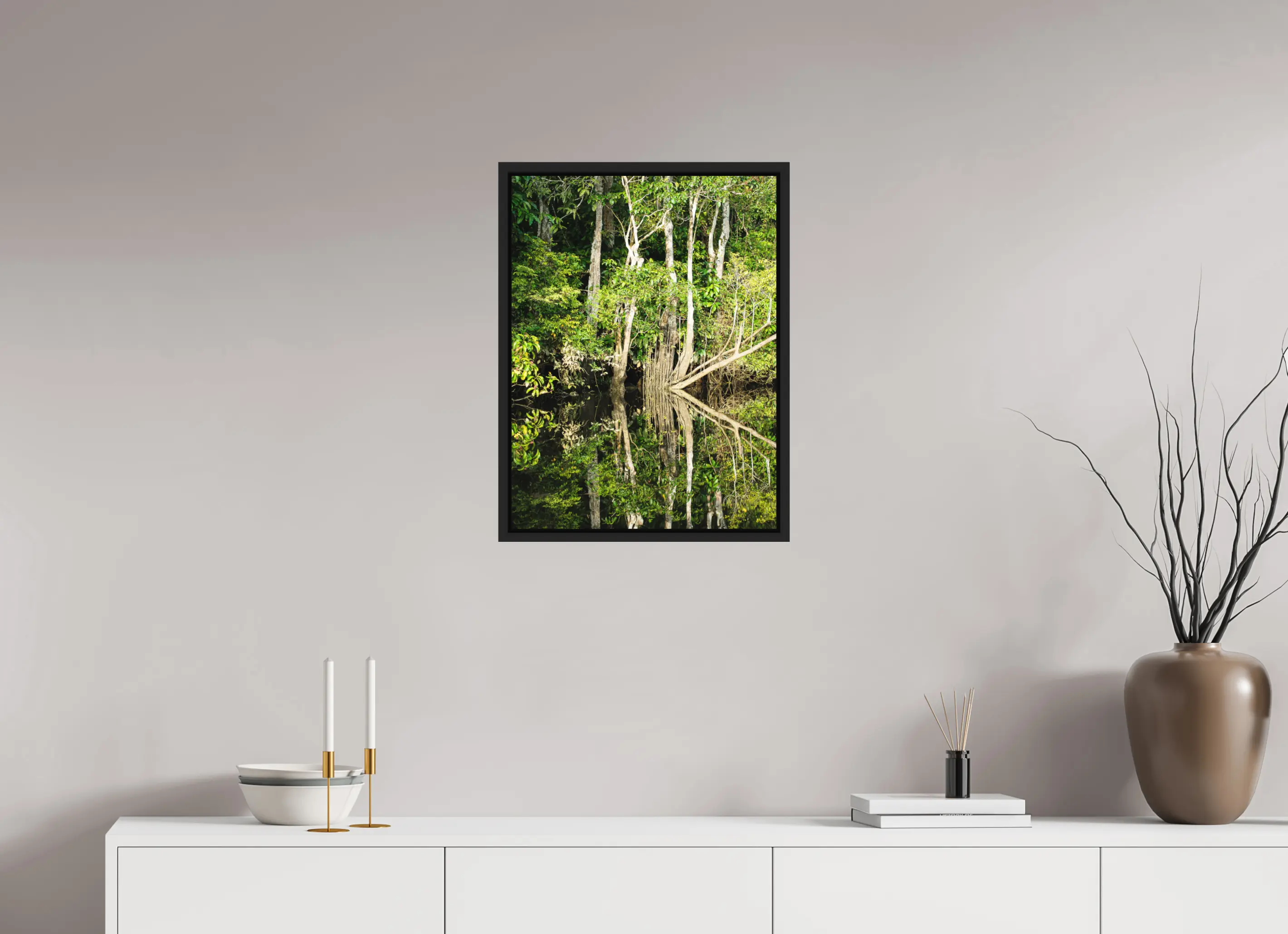 Fine art print “The Jungle Mirror” featuring dense Bornean rainforest trees perfectly reflected in still dark river water, displayed in a floater frame in a modern living room setting.
