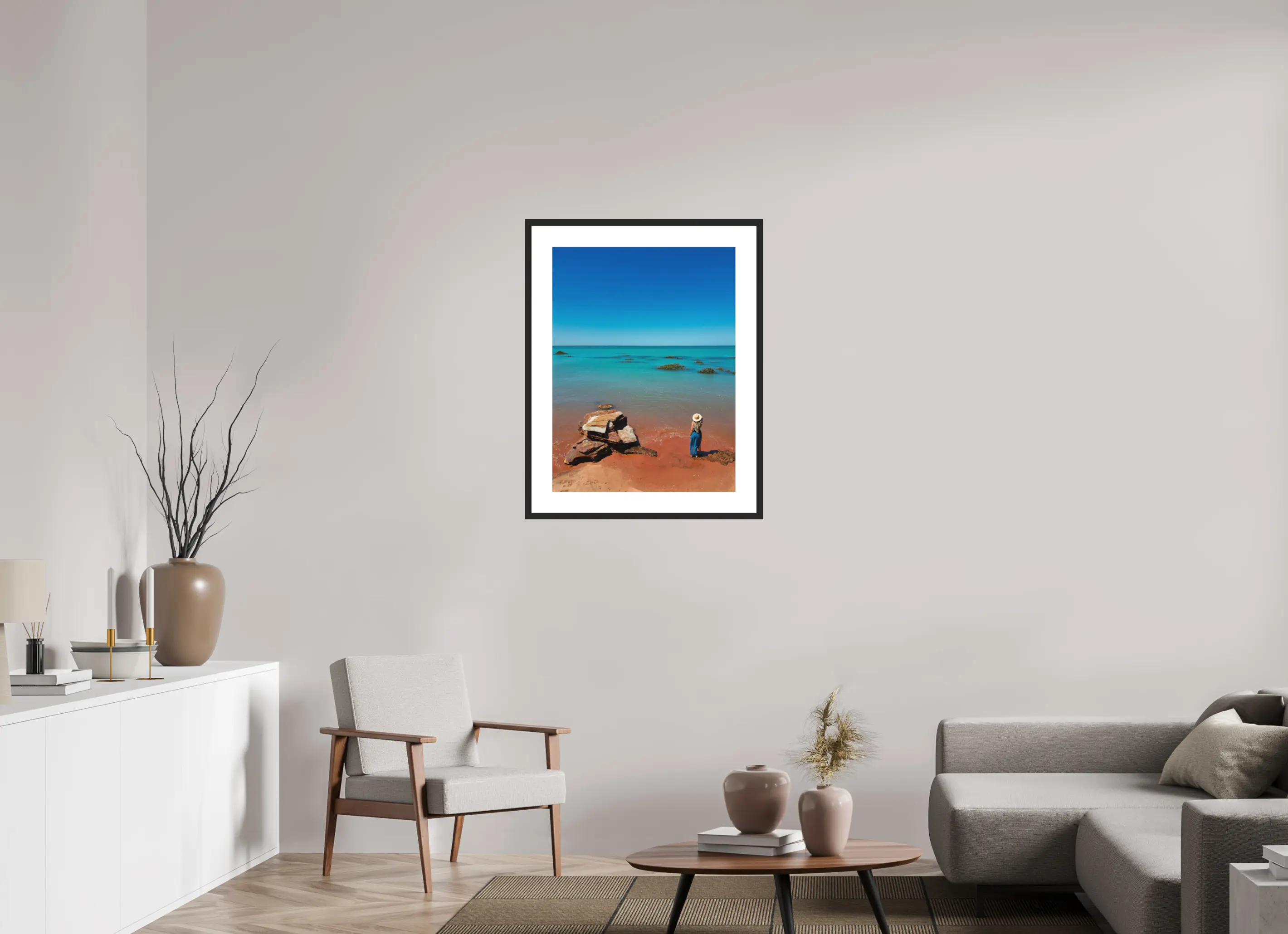 Fine art print “Desert meets the Sea” featuring a woman standing on red sand beach in Broome Western Australia gazing over turquoise ocean waters, displayed in a passepartout frame in a modern living room setting.