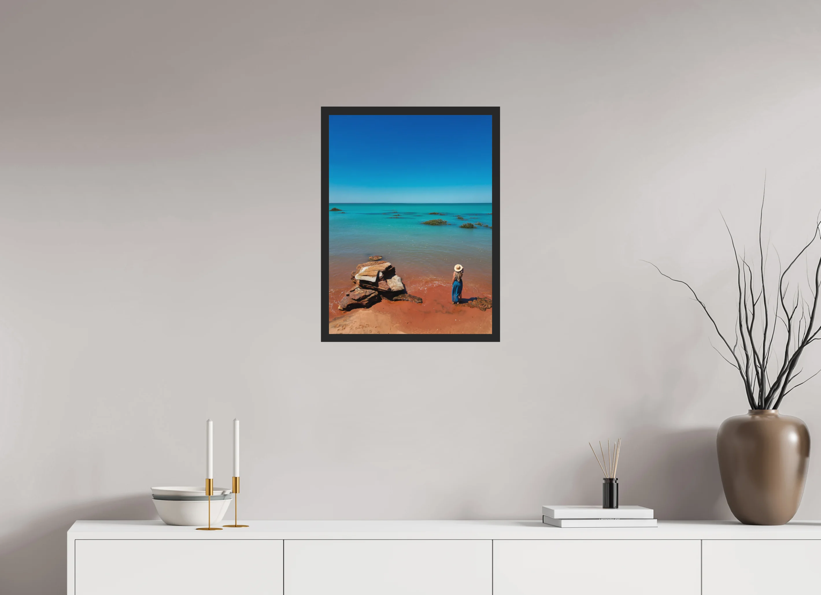Fine art print “Desert meets the Sea” featuring a woman standing on red sand beach in Broome Western Australia gazing over turquoise ocean waters, displayed classic framed in a modern living room setting.
