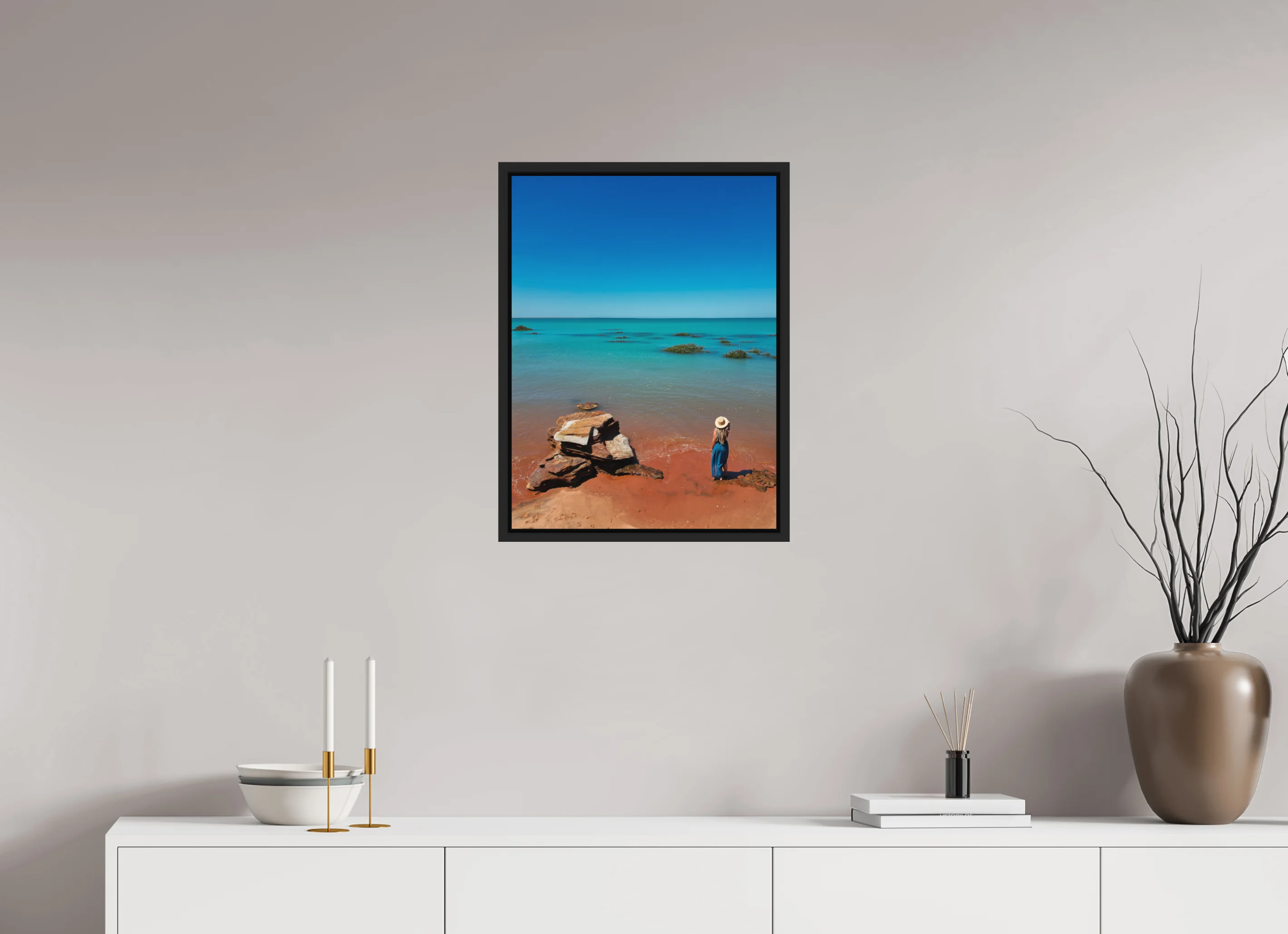 Fine art print “Desert meets the Sea” featuring a woman standing on red sand beach in Broome Western Australia gazing over turquoise ocean waters, displayed in a floater frame in a modern living room setting.