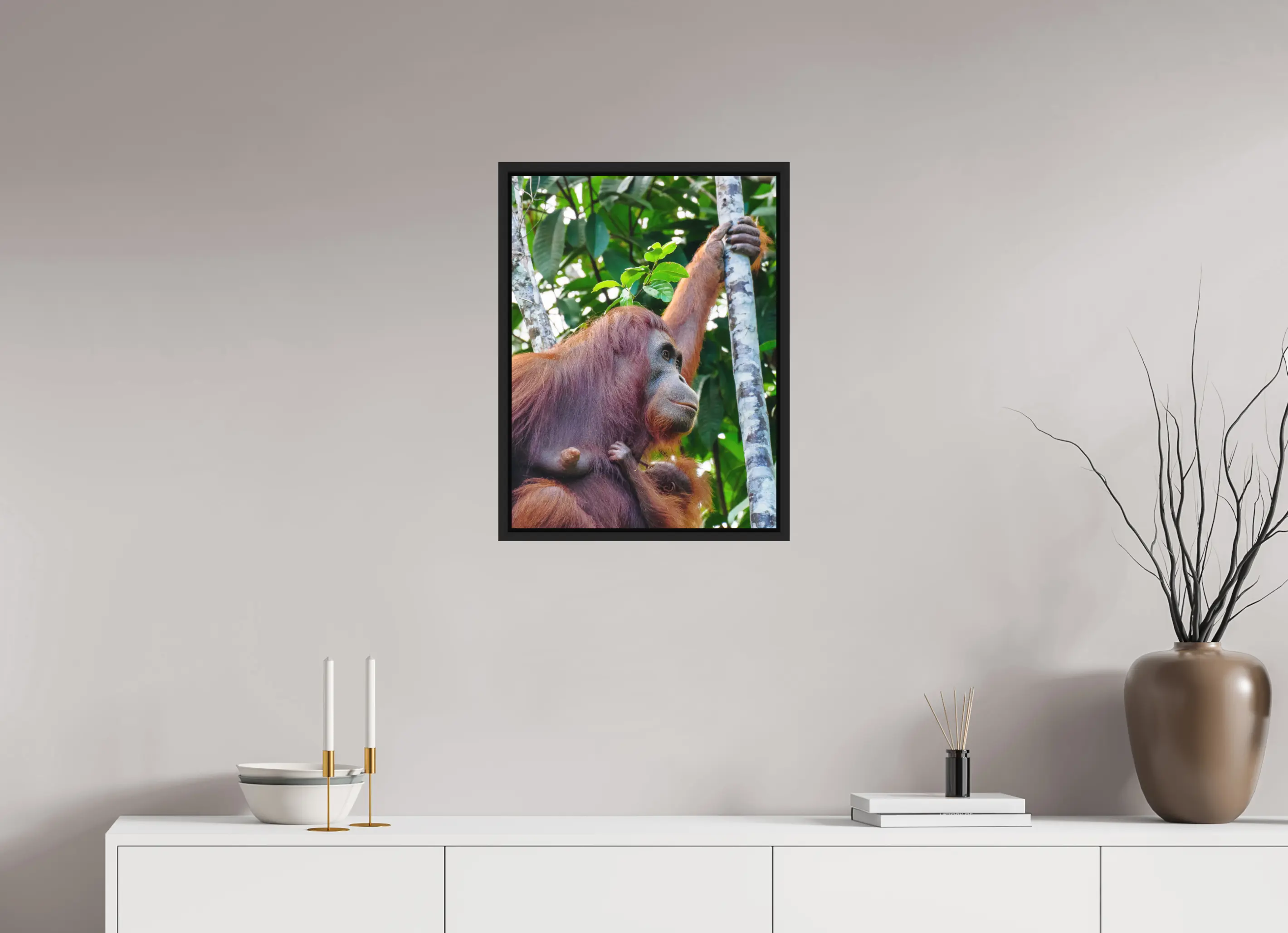 Fine art print “Motherhood” featuring a orangutan holding her baby in the tropical rainforest canopy of Borneo, displayed in a floater frame in a modern living room setting.