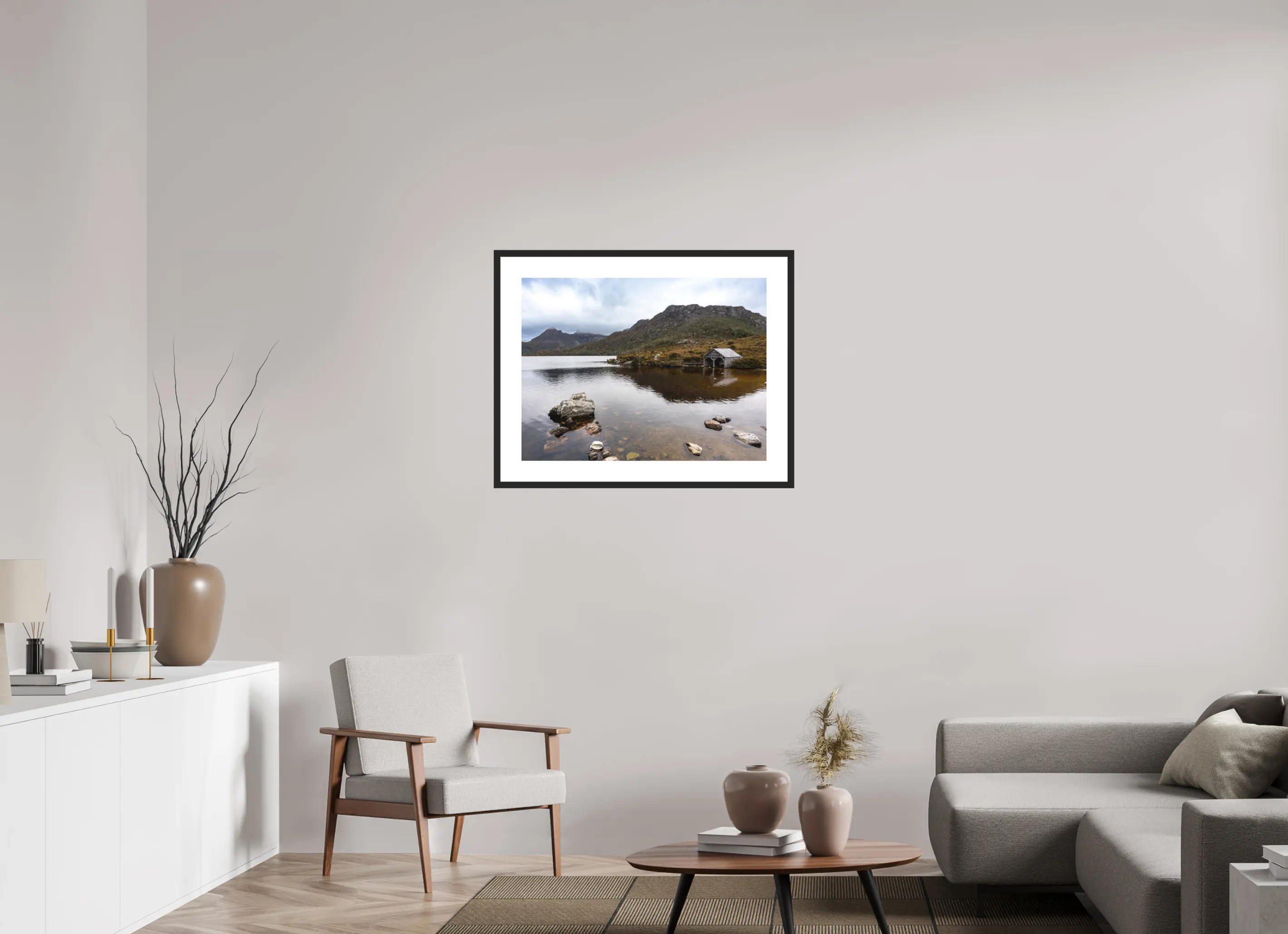 Fine art print “Presence” featuring a wooden boathouse on the calm waters of Dove Lake beneath Cradle Mountain in Tasmania, displayed in a passepartout frame in a modern living room setting.