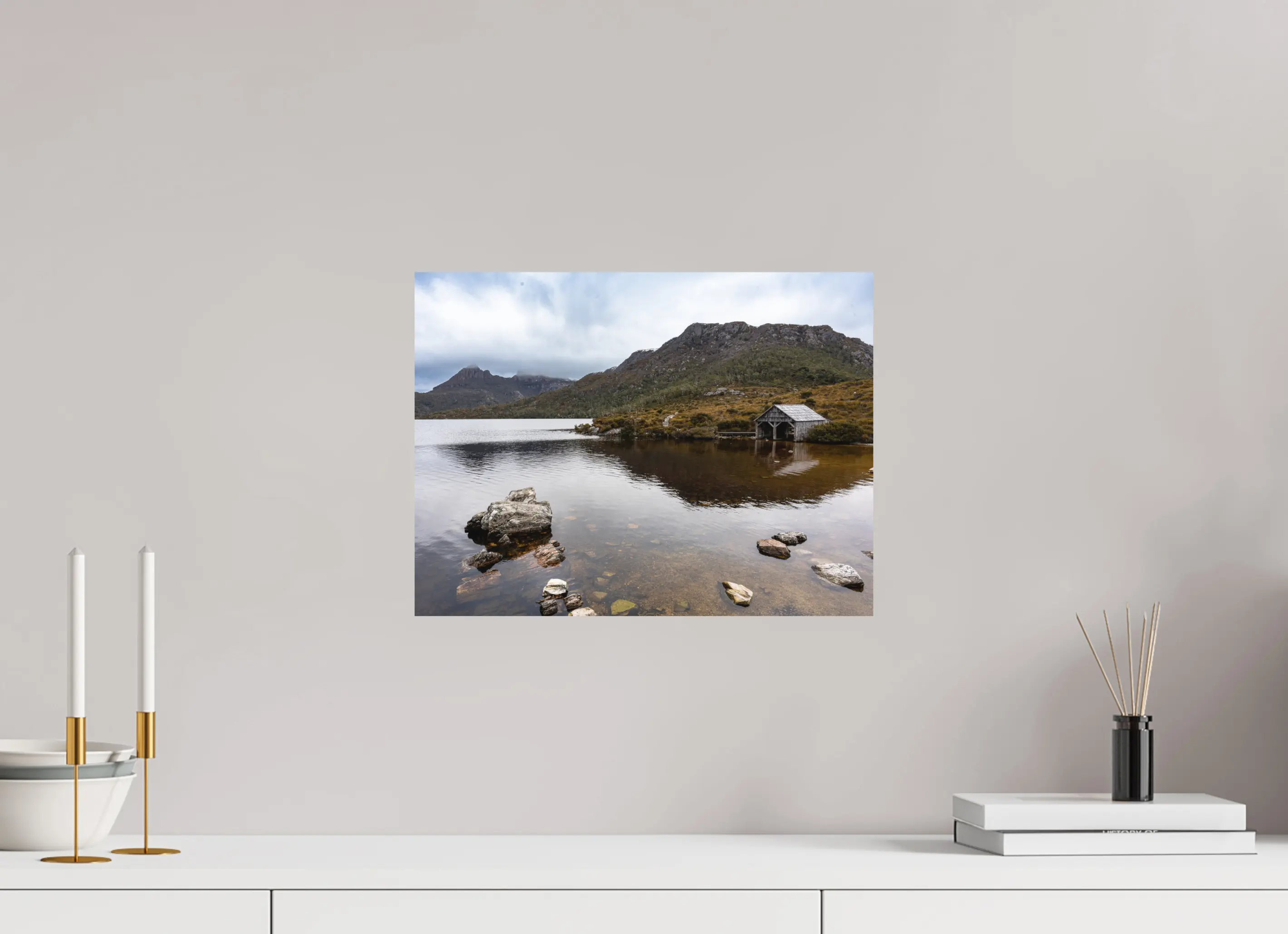 Fine art print “Presence” featuring a wooden boathouse on the calm waters of Dove Lake beneath Cradle Mountain in Tasmania, displayed on aluminium dibond in a modern living room setting.
