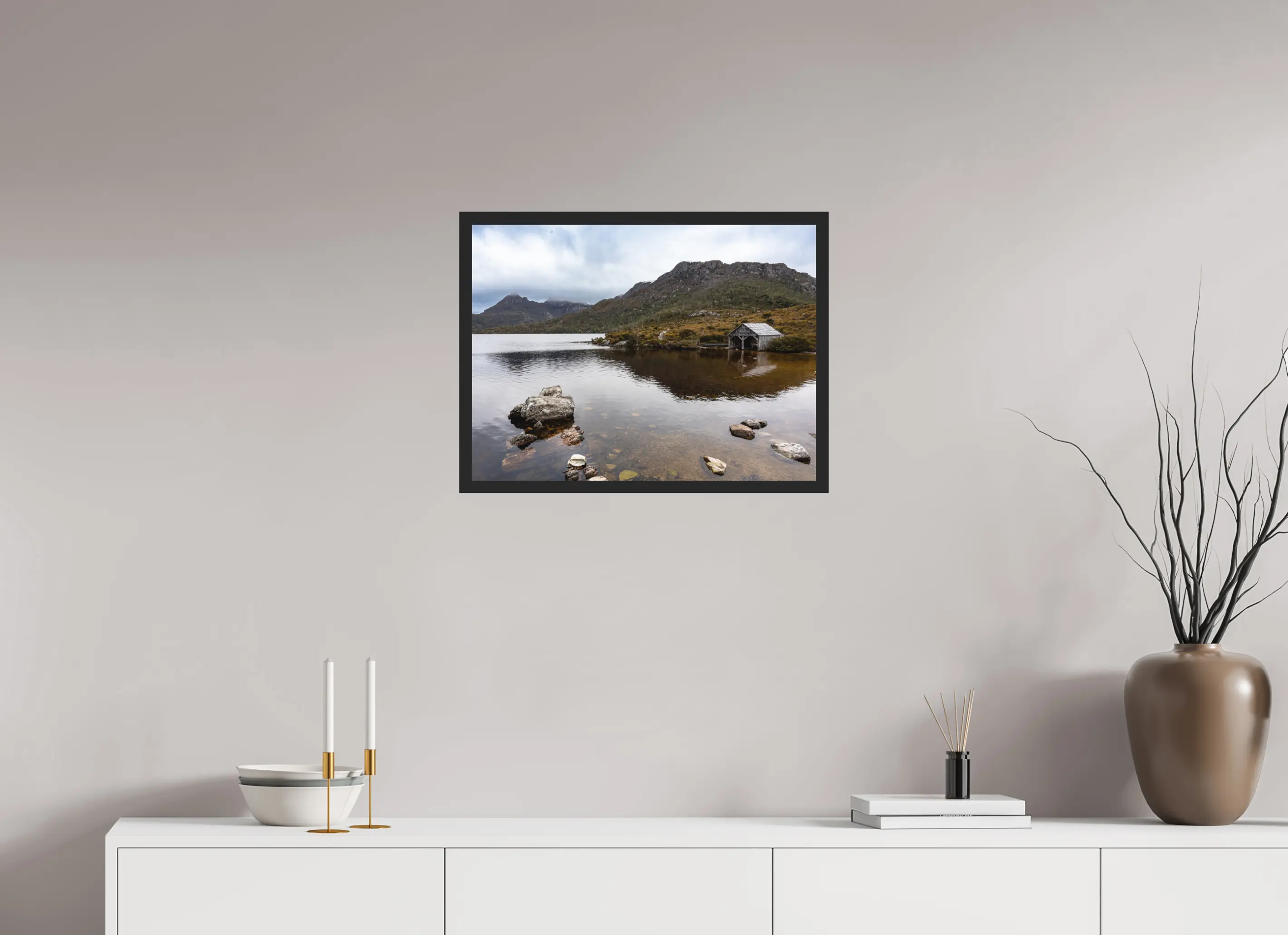 Fine art print “Presence” featuring a wooden boathouse on the calm waters of Dove Lake beneath Cradle Mountain in Tasmania, displayed classic framed in a modern living room setting.