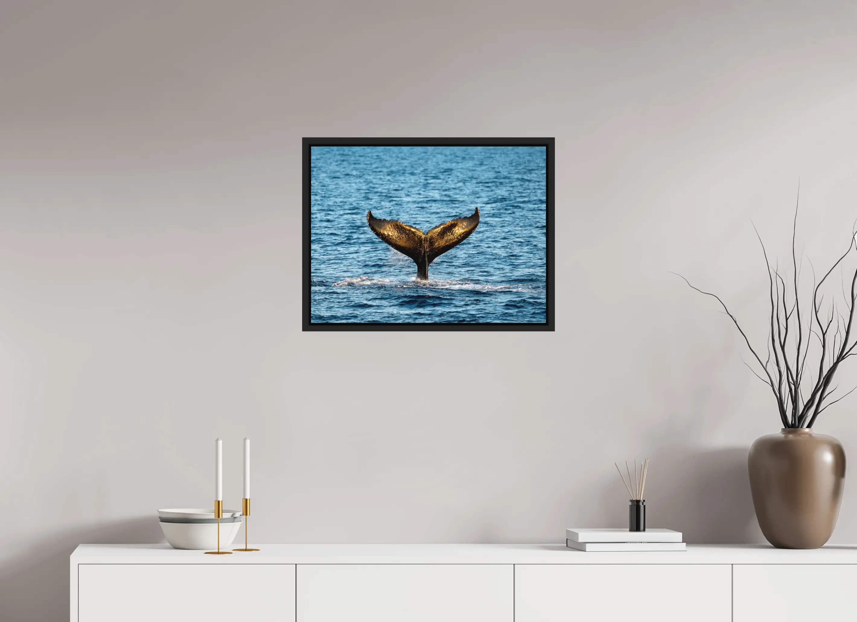 Fine art print “The Golden Fluke” featuring a humpback whale tail reflecting golden sunlight as it dives into the blue ocean, displayed in a floater frame in a modern living room setting.