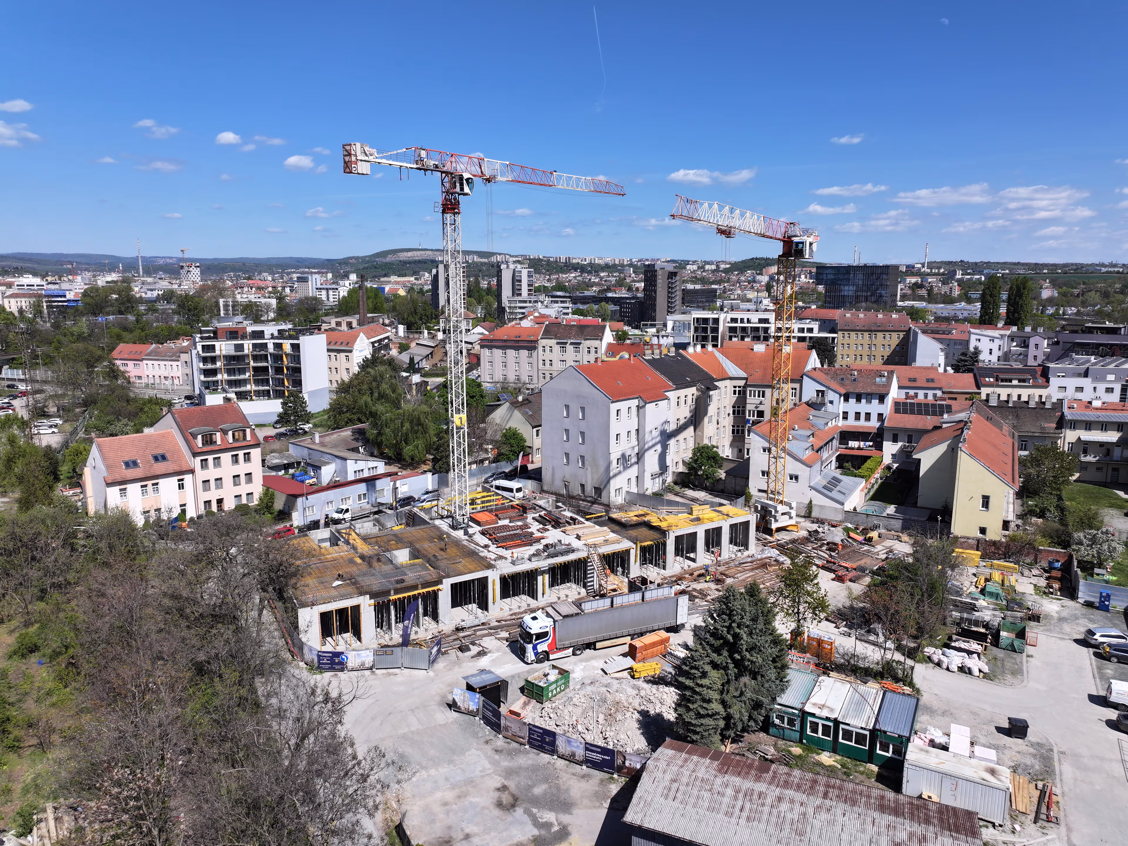 Stavební plocha s jeřáby a kamiony v městské oblasti za slunného dne.
