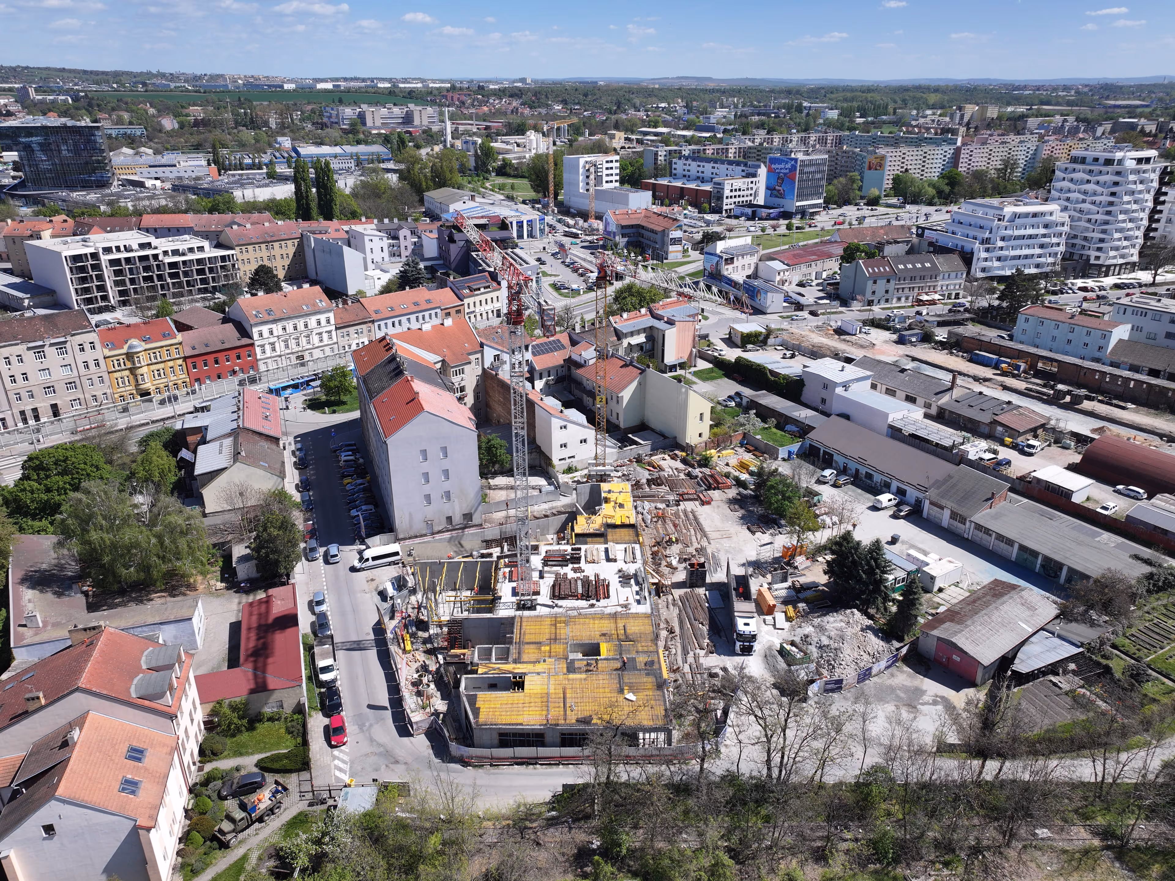Letecký pohled na stavební projekt s jeřáby a okolními budovami ve městě během dne.