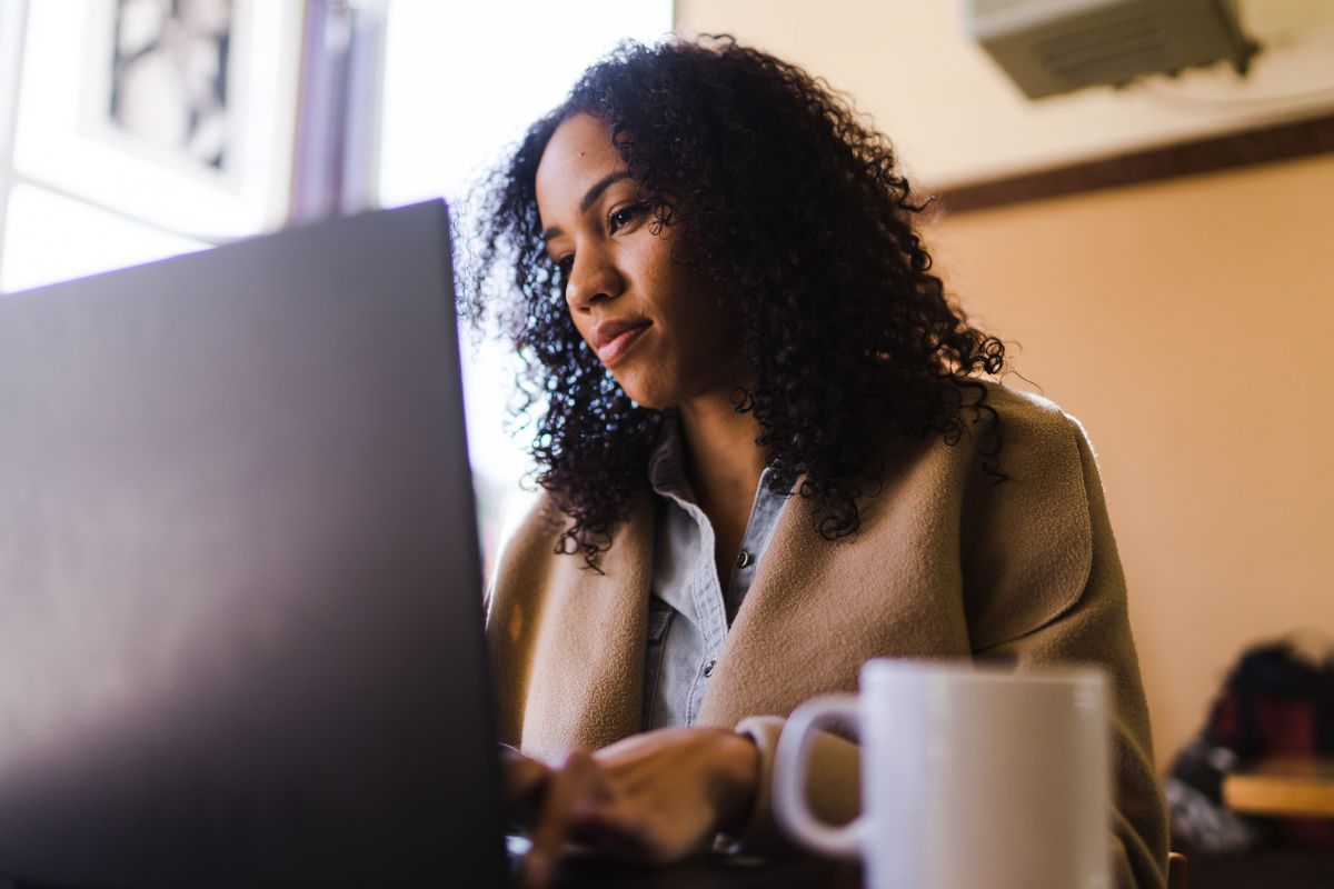 HR professional reviewing I-9 compliance documents on laptop with coffee mug, ensuring proper verification of acceptable employment authorization records.