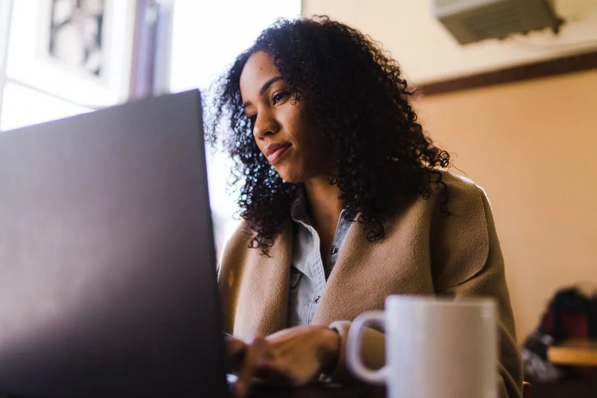 HR professional reviewing I-9 compliance documents on laptop with coffee mug, ensuring proper verification of acceptable employment authorization records.