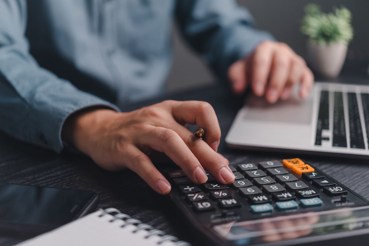 HR professional calculating I-9 compliance exposure using a calculator and laptop to assess audit fines and workforce risk.