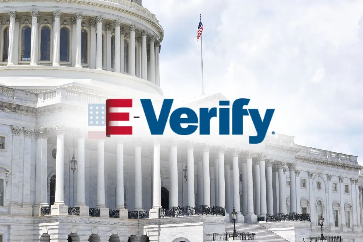 The U.S. Capitol building with an overlaid E-Verify logo in the center. The image symbolizes the intersection of federal government authority and employment eligibility verification under the E-Verify system.