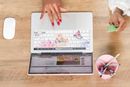 Aerial view of a person using a credit card to make a purchase on an e-commerce product page. Their open laptop is resting on a wooden surface next to a pink pencil holder and Apple magic mouse.