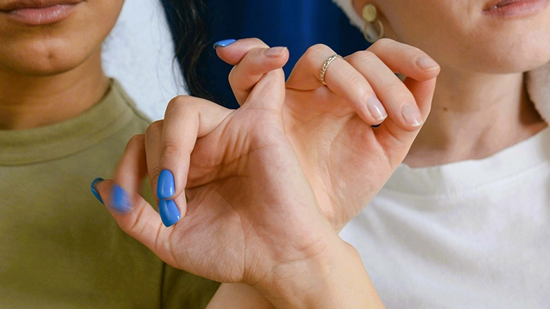 Close-up of two people seated side-by-side, locking their pinky fingers together in a pinky swear.