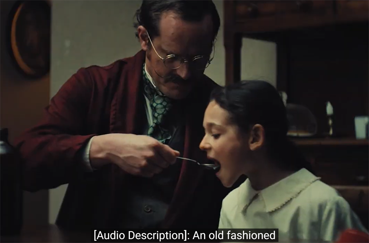 Campaign still frame a doctor spooning liquid into a young girl's mouth. Caption reads, "[Audio Description]: An old fashioned..."