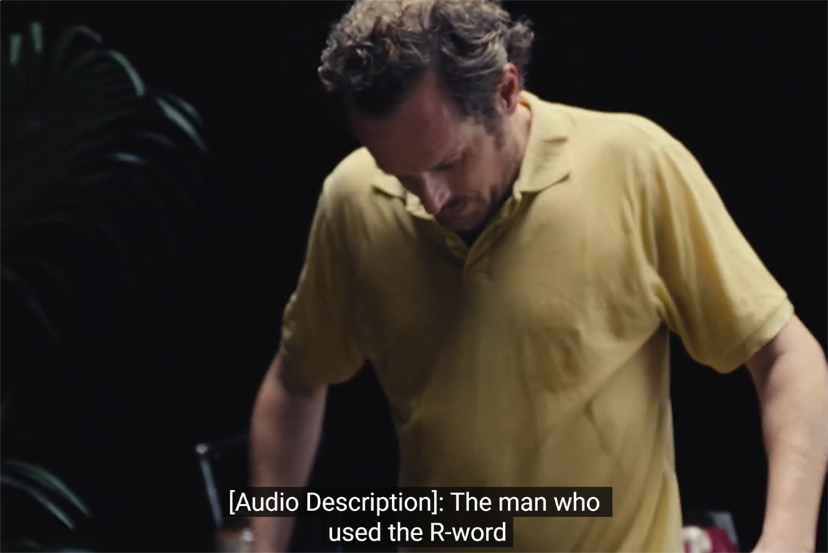 Campaign still frame shows the man who used the R-Word looking down at a yellow polo shirt. Caption reads, "[Audio Description]: The man who used the R-word..."