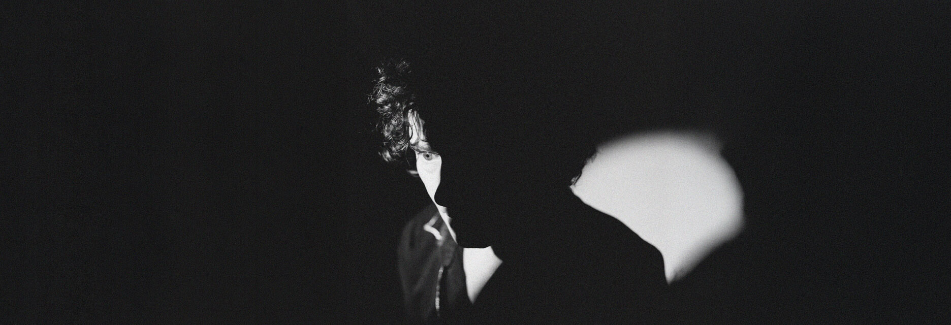 Black and white portrait of Enrique Bunbury partially illuminated against a dark background.