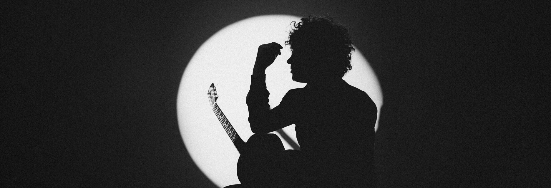 Black and white silhouette of Enrique Bunbury holding a guitar against a circular spotlight background.