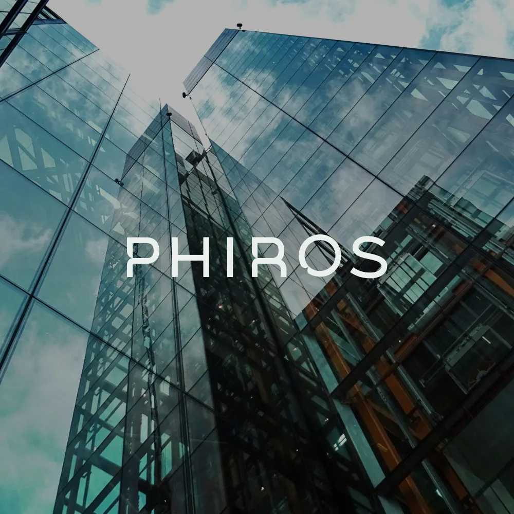 Looking up at tall glass skyscrapers reflecting a cloudy sky with the word PHIROS overlaid.