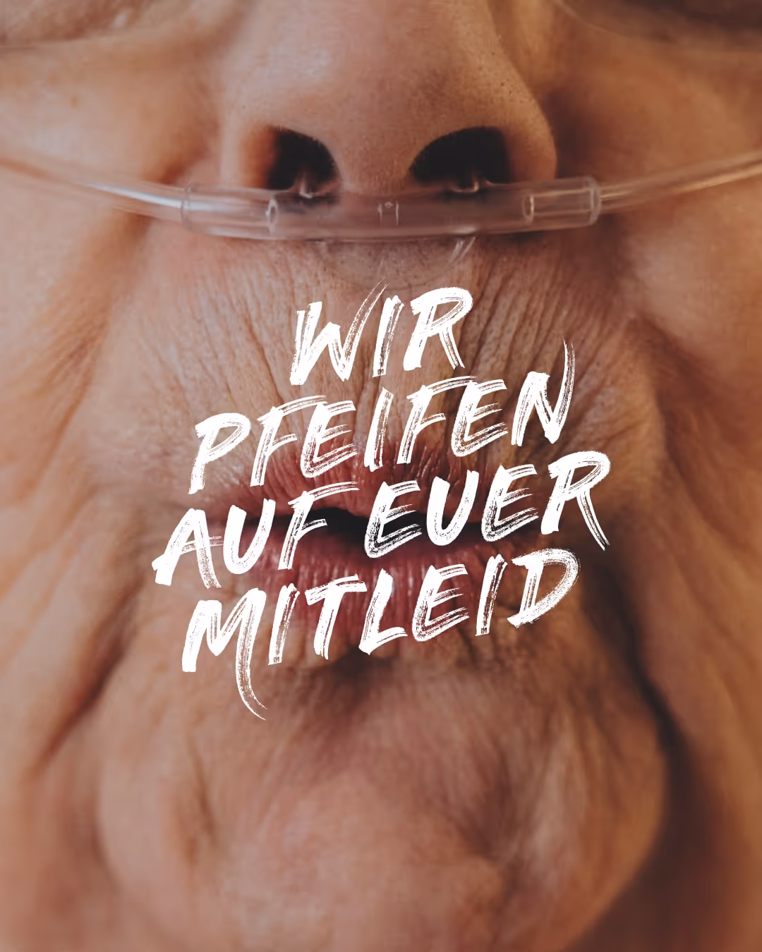Nahaufnahme des Gesichts einer älteren Person mit Sauerstoffbrille. Die Lippen sind zum Pfeifen geformt. Darüber steht in weißer, ausdrucksstarker Pinseltypografie: ‚Wir pfeifen auf euer Mitleid‘.