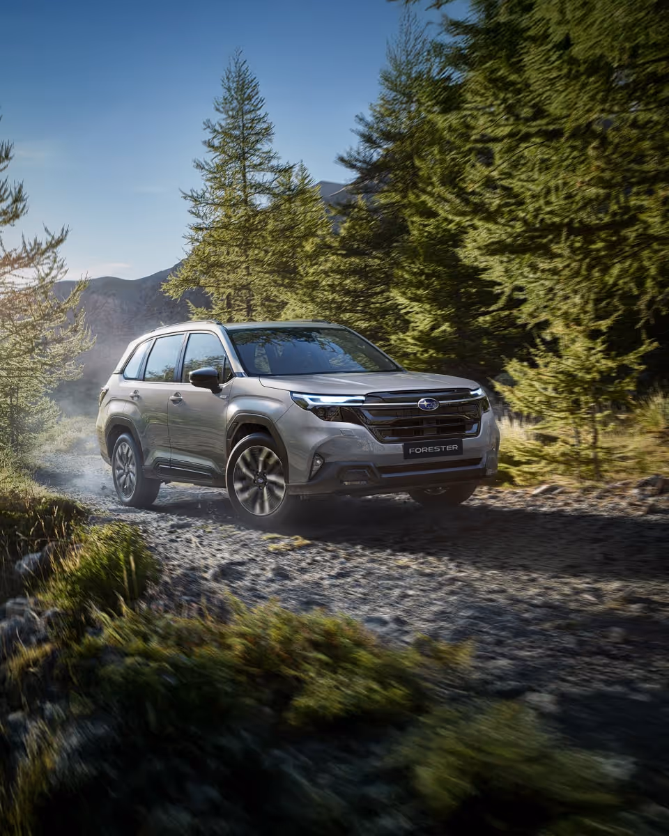 Subaru Forester driving through muddy terrain in front of a dramatic mountain backdrop; the vehicle kicks up mud, emphasizing its off-road capabilities.