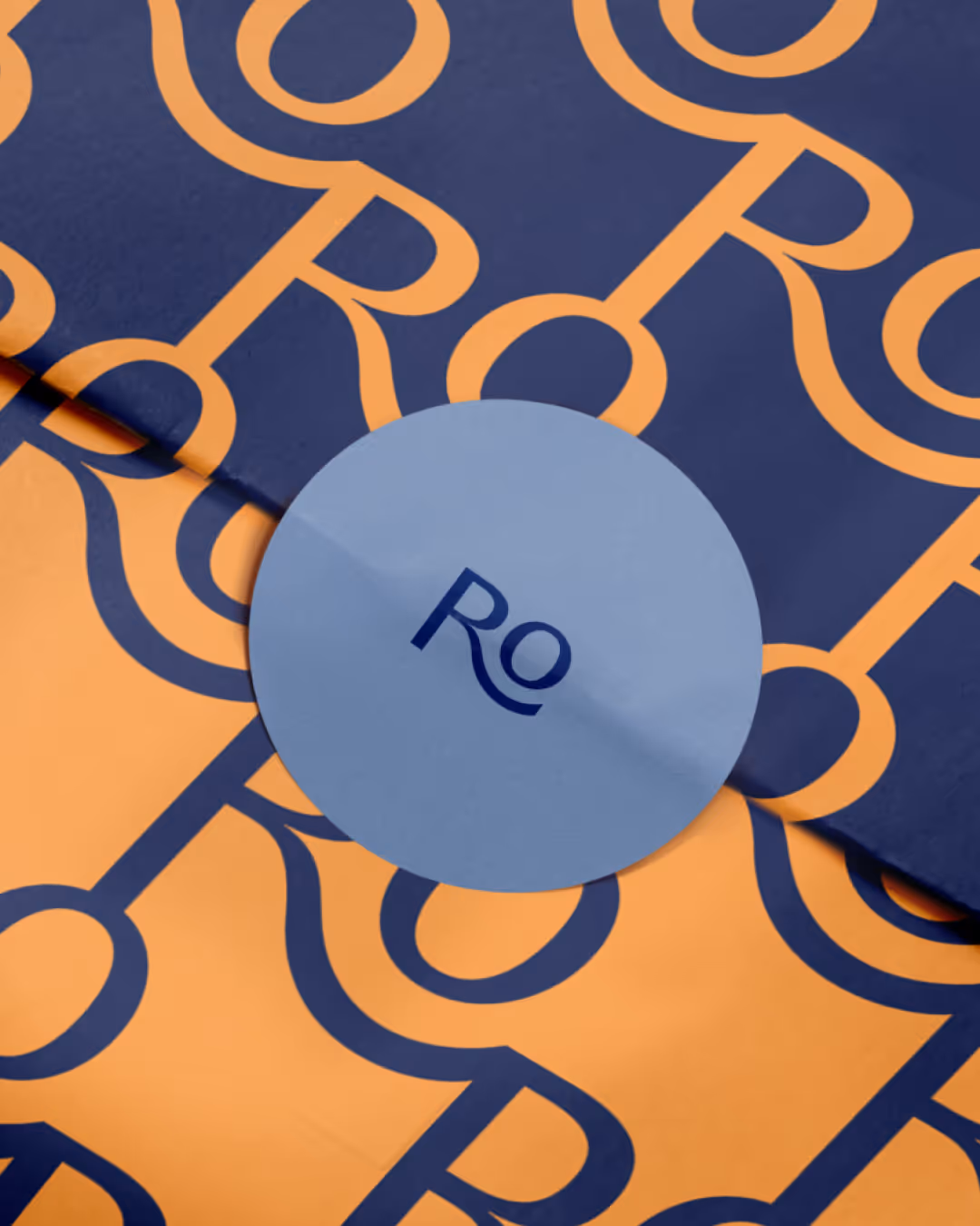 Close-up view of Rondoro packaging with stylized monogram pattern in orange on dark blue and round blue sticker with brand logo.