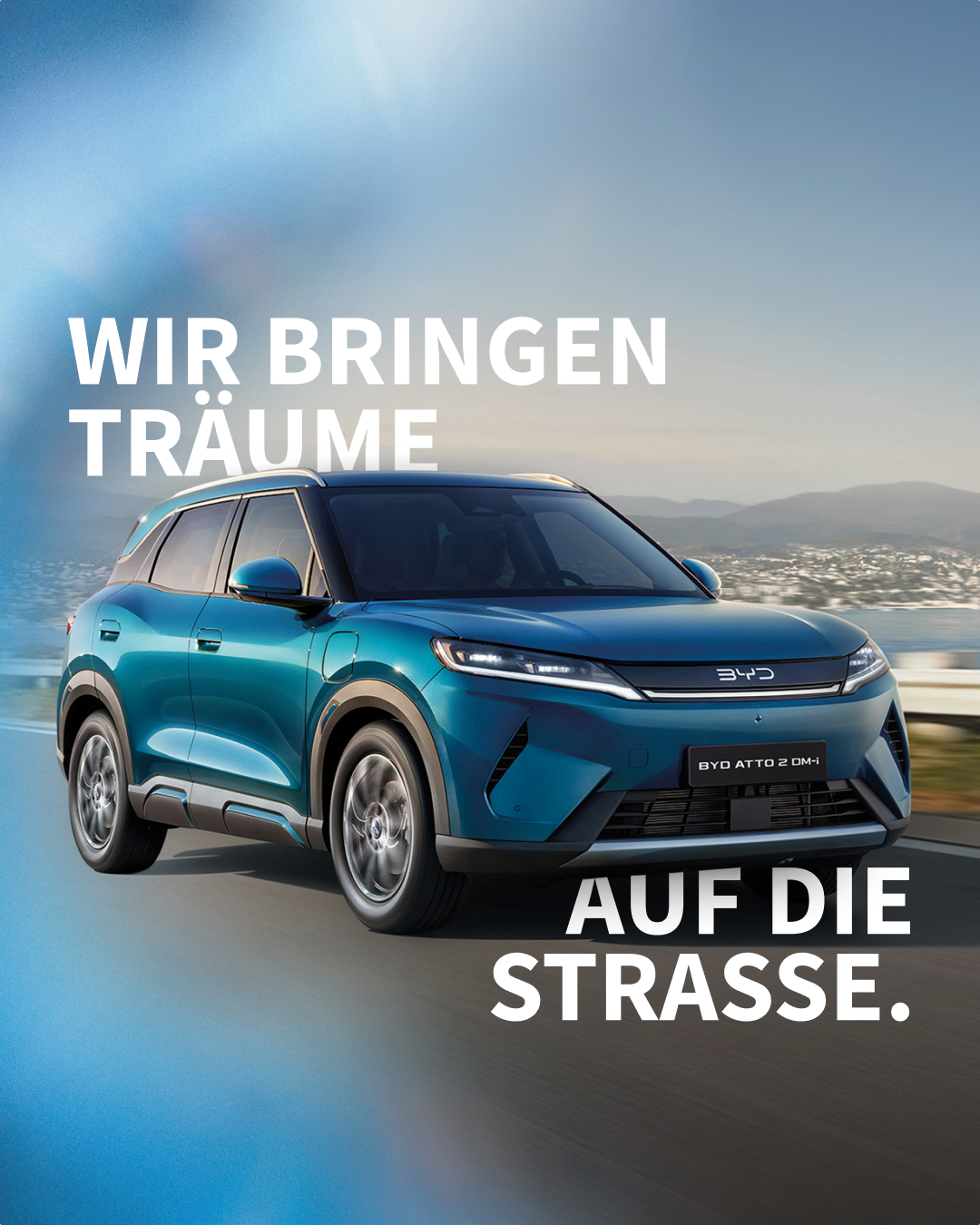 BYD ATTO 2 DM-i in Fahrt auf einer Küstenstraße, mit dem Claim „Wir bringen Träume auf die Straße.“