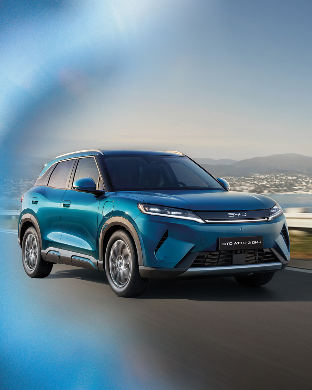 BYD ATTO 2 DM-i in Fahrt auf einer Küstenstraße, mit dem Claim „Wir bringen Träume auf die Straße.“