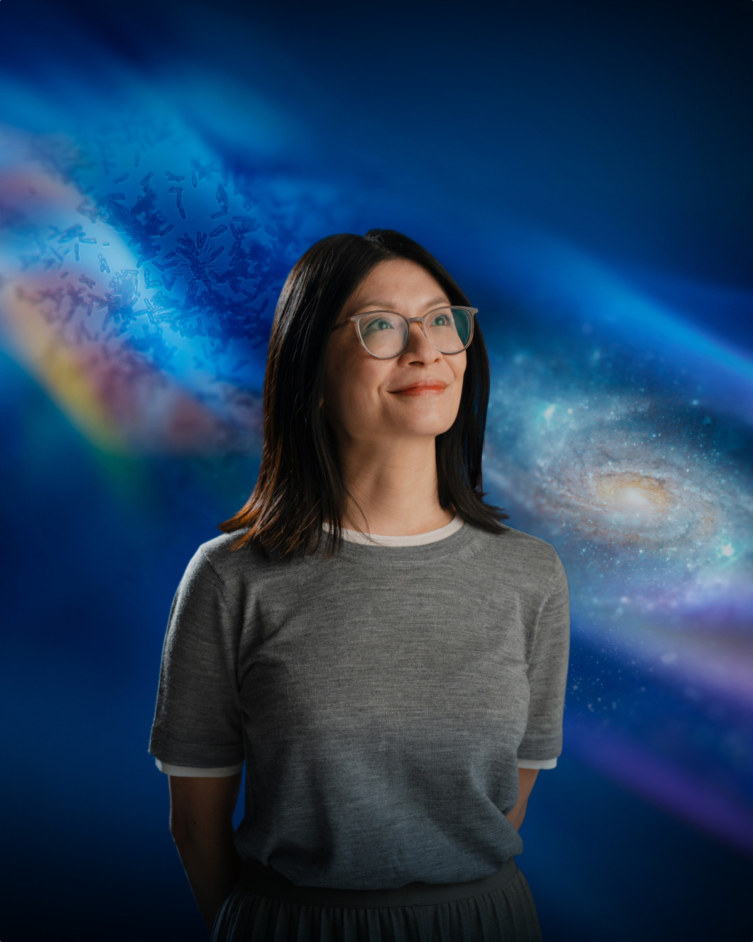 Porträt einer Frau mit Brille vor einer blauen Collage aus mikroskopischen Strukturen, Galaxie und abstrakten Lichtwelten.